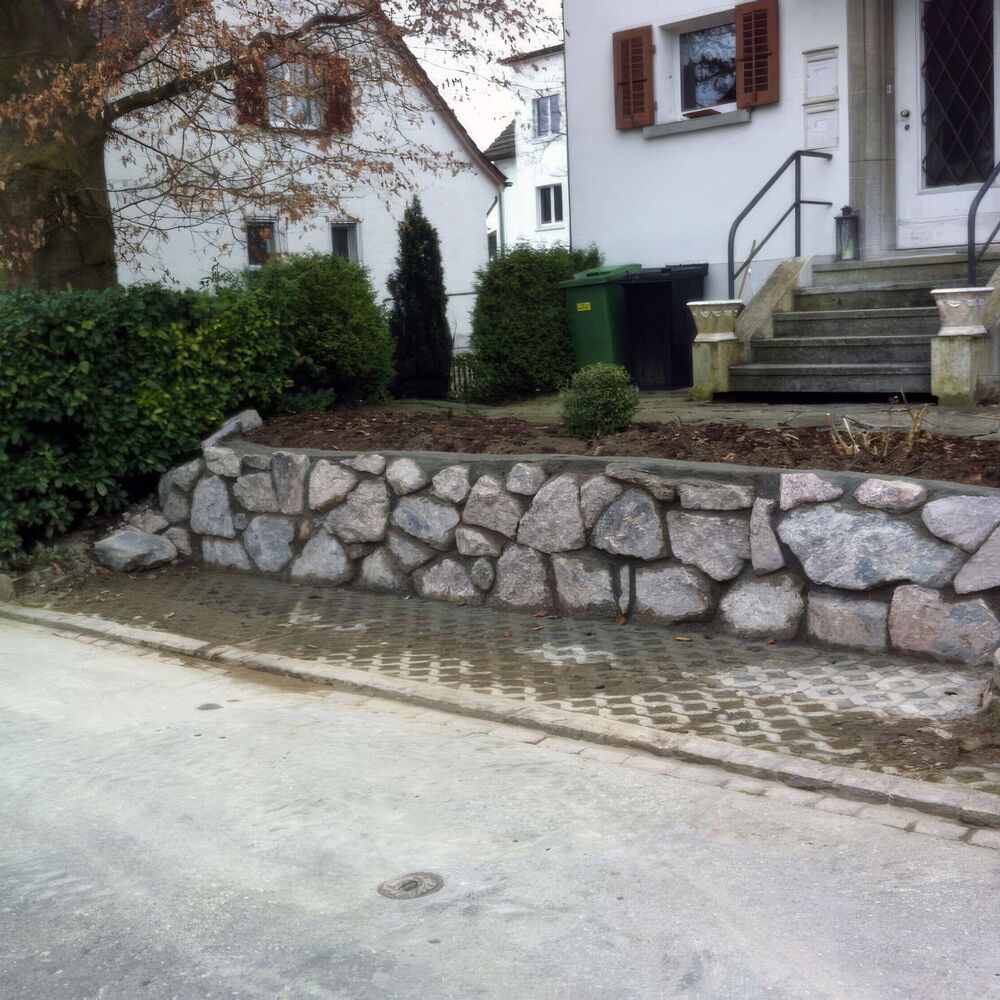 Natursteinmauer mit Gartenbepflanzung vor einem Wohnhaus